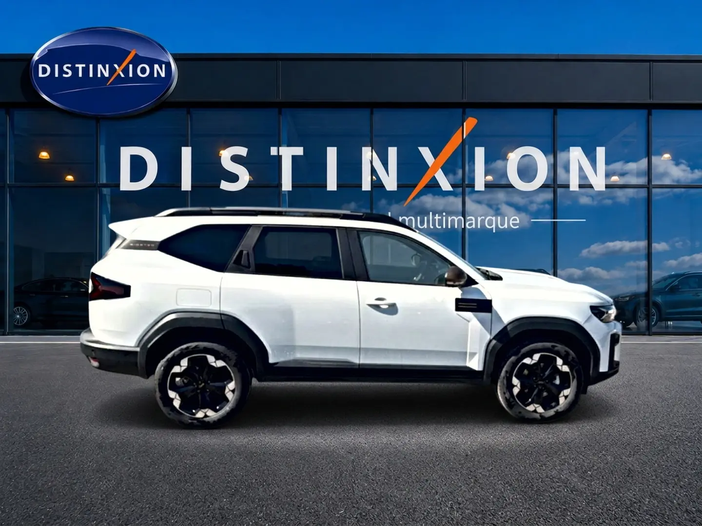 Profil droit du SUV blanc Dacia Bigster 2026 avec jantes noires et toit panoramique devant une vitrine Distinxion.
