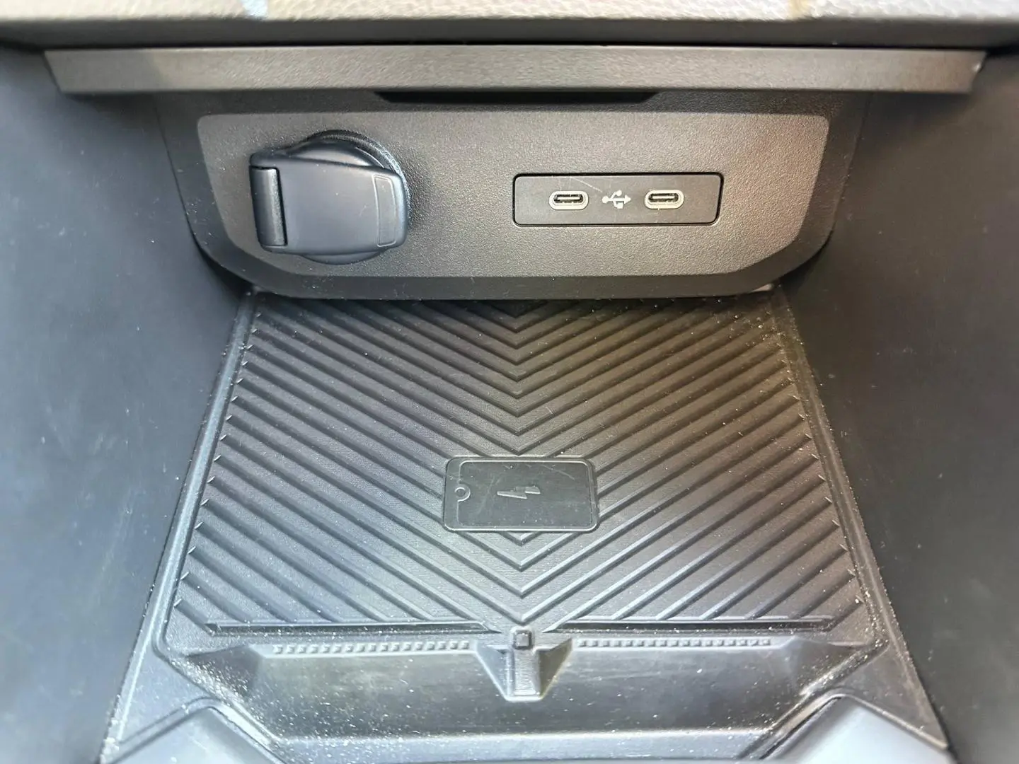 Gros plan sur la console centrale du Dacia Duster 2025 avec prise 12V, deux ports USB-C et surface de charge sans fil noire.