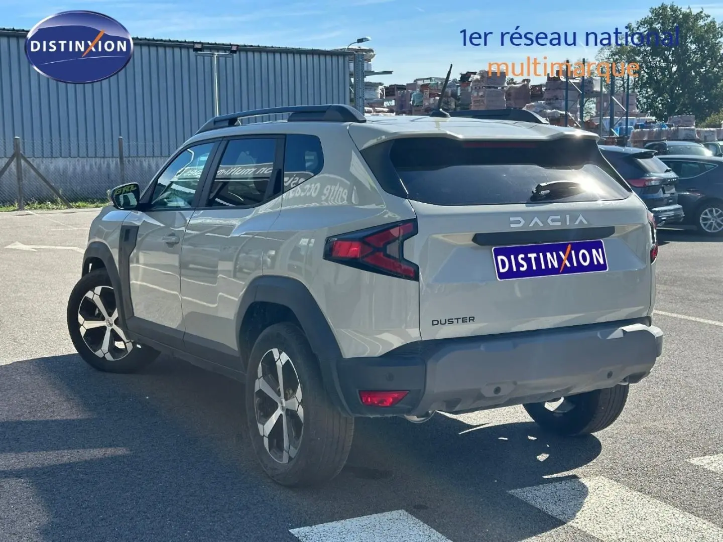 Vue 3/4 arrière droite du Dacia Duster 2025 couleur Sandstone avec barres de toit et jantes alu distinctives.