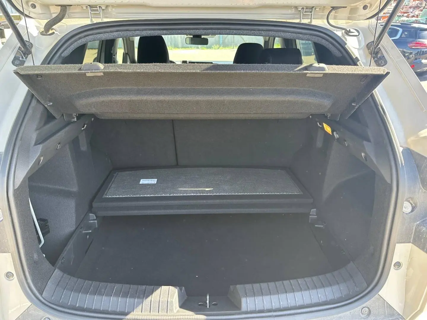 Coffre ouvert du Dacia Duster 2025 couleur Sandstone, montrant le plancher de coffre mobile et la tablette cache-bagages.