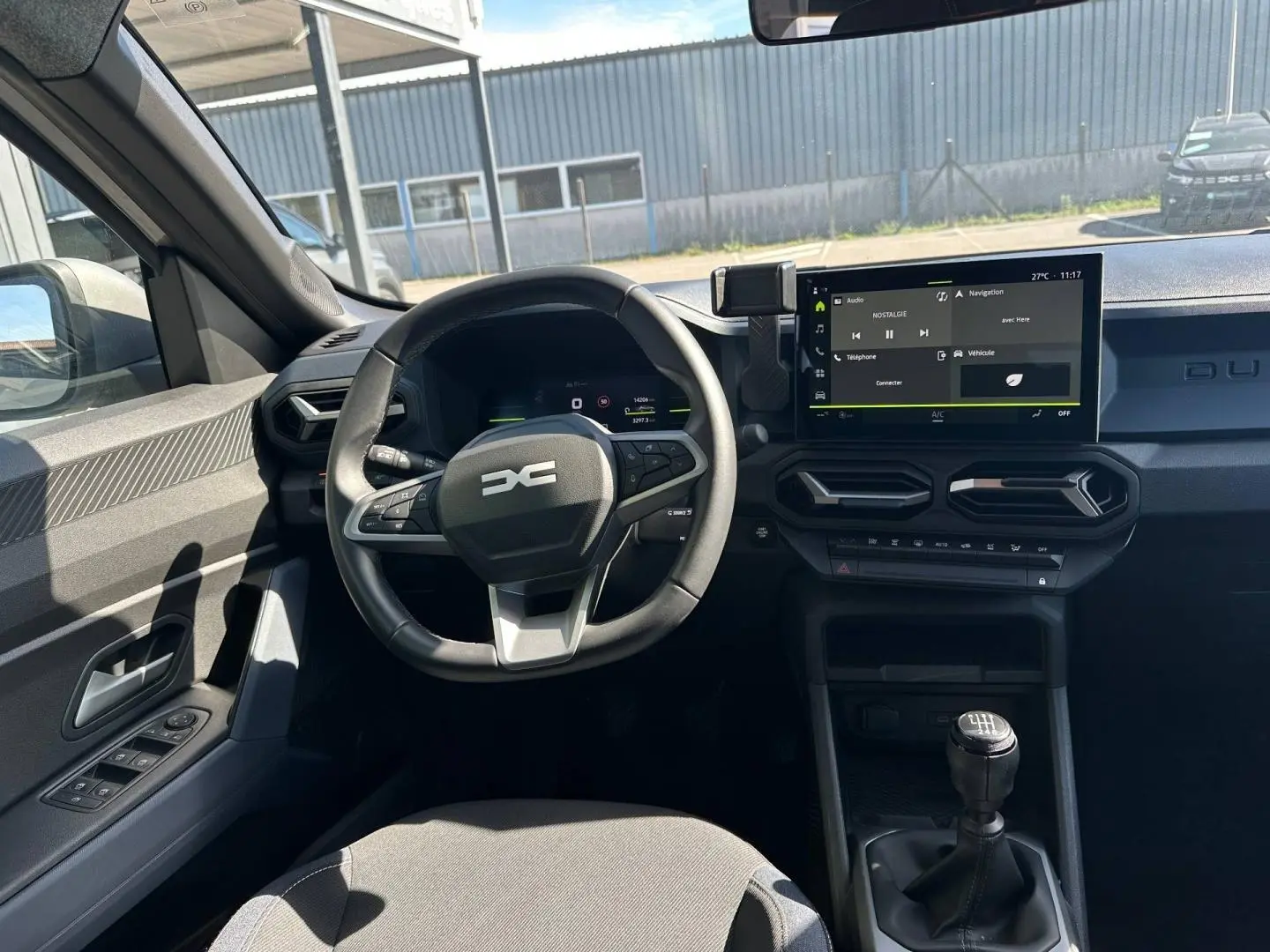 Vue intérieure côté conducteur du Dacia Duster 2025 avec volant multifonction, écran tactile et levier de vitesse manuel.