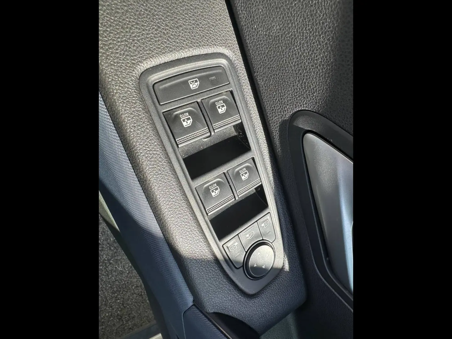 Vue rapprochée des commandes de lève-vitres et réglage des rétroviseurs sur la porte côté conducteur du Dacia Duster Sandstone.