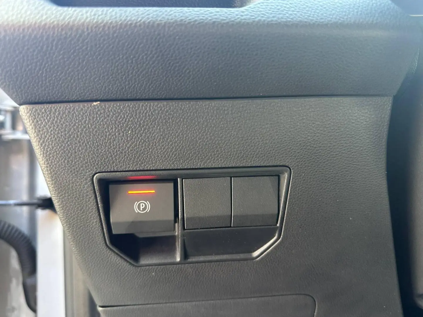 Détail du bouton de frein de stationnement électronique allumé sur le tableau de bord noir du Dacia Duster 2025.