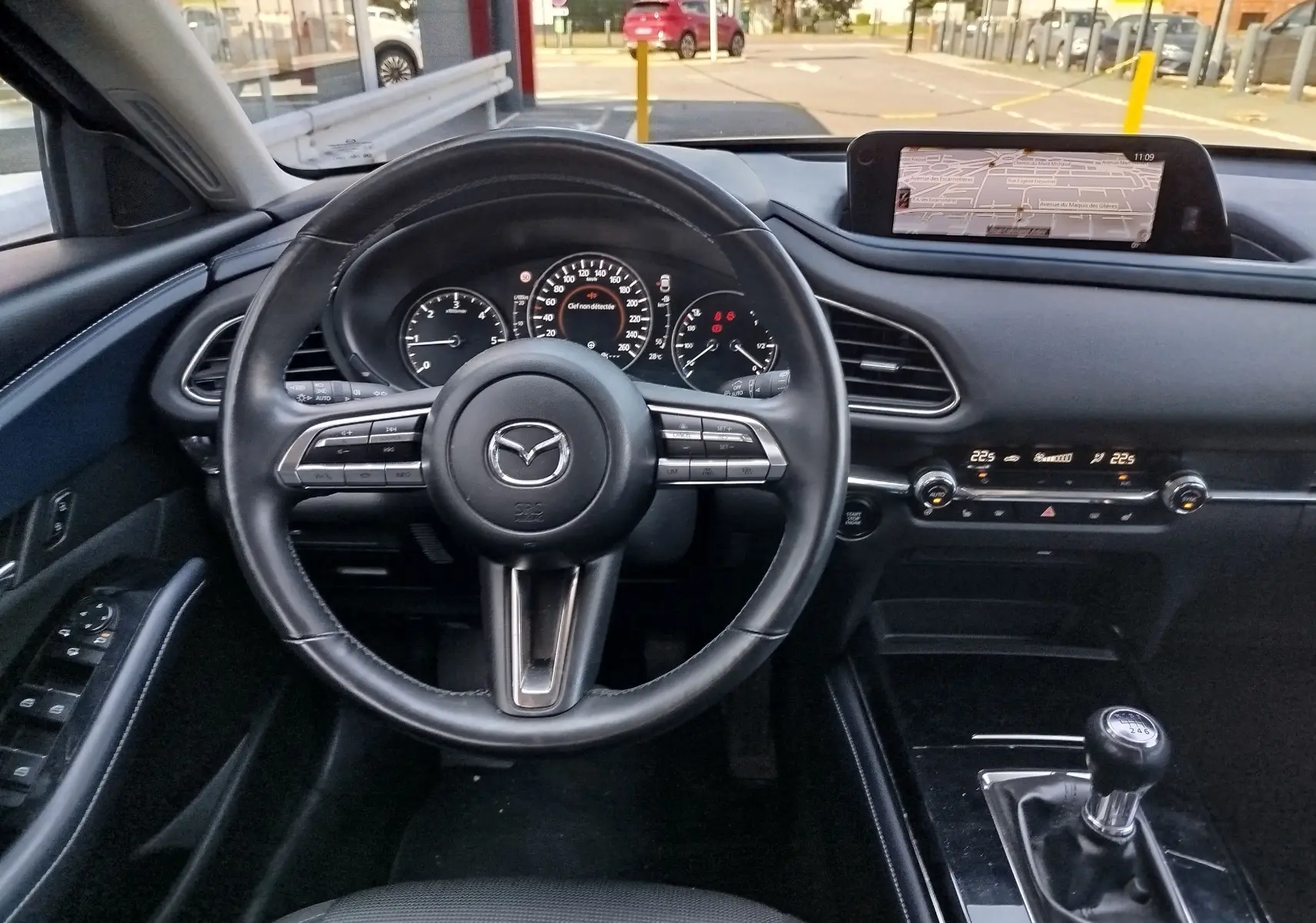 Vue intérieure du poste de conduite du Mazda CX-30 noir de 2020, avec volant cuir, tableau de bord digital et levier de vitesse manuel.