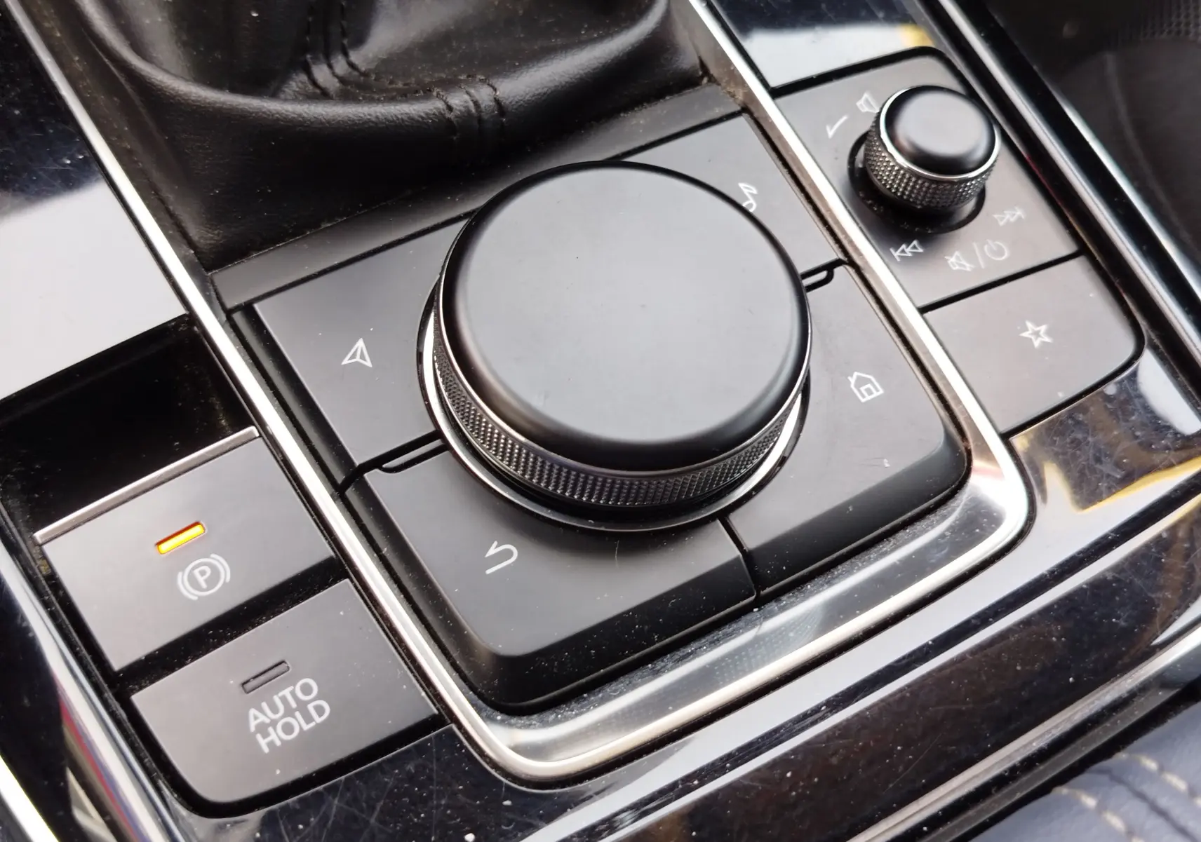 Gros plan sur la molette de commande centrale noire et les boutons environnants dans l'habitacle du Mazda CX-30 noir.