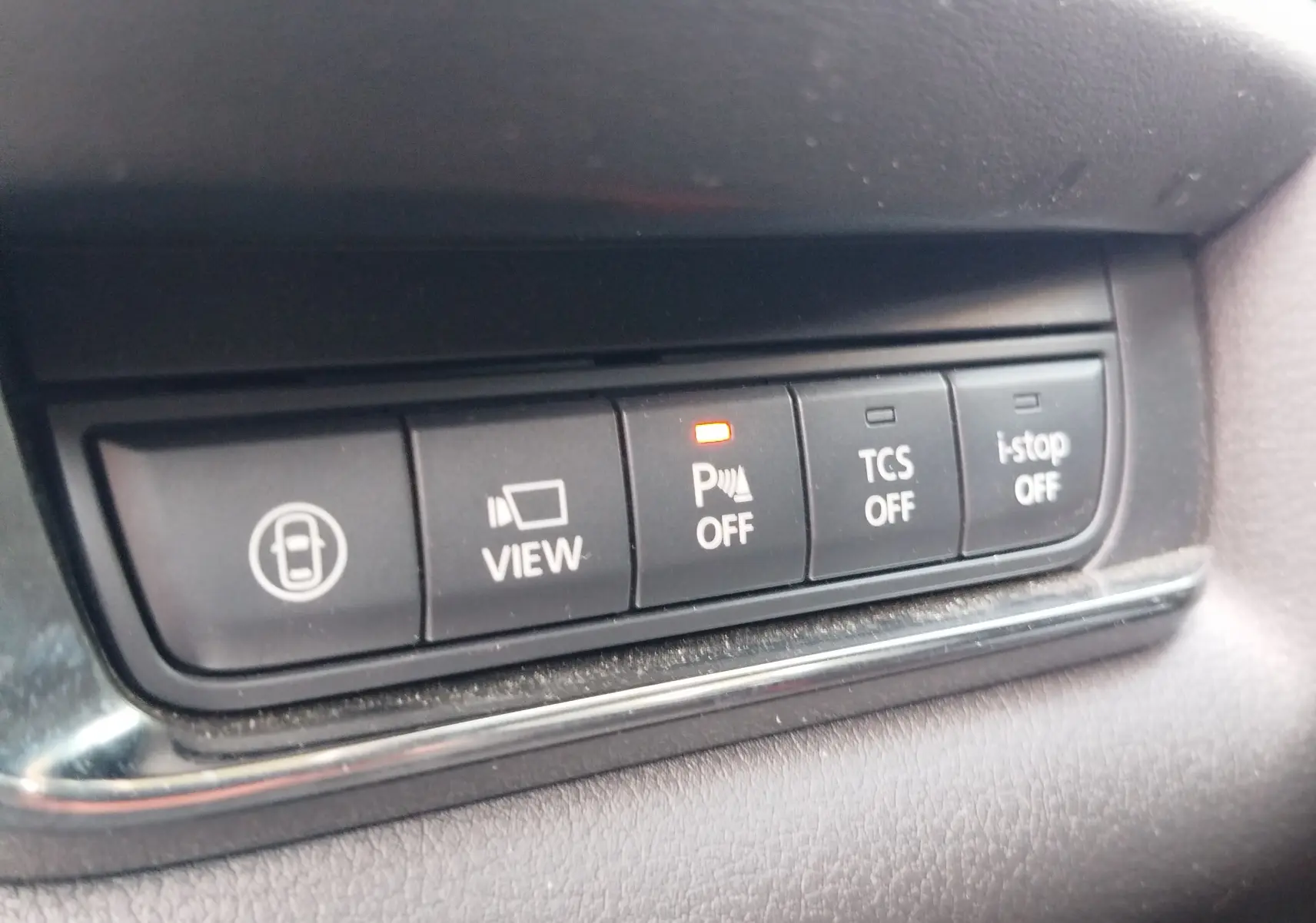 Gros plan sur les boutons de commande intérieurs du Mazda CX-30 noir 2020, avec témoin orange allumé sur le bouton de stationnement assisté.