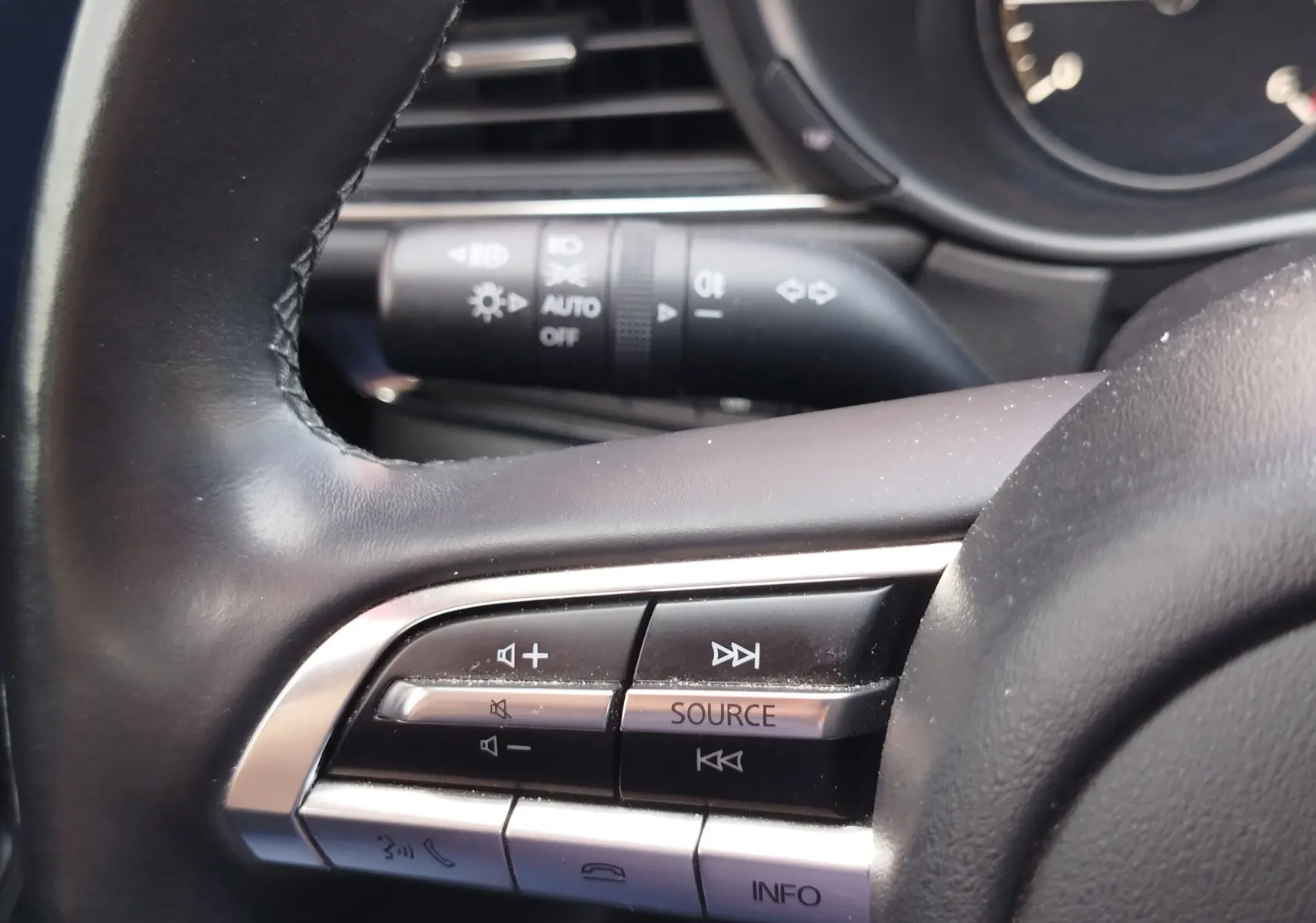 Gros plan sur les commandes audio au volant d'un Mazda CX-30 noir, avec boutons de volume et source sonore visibles.