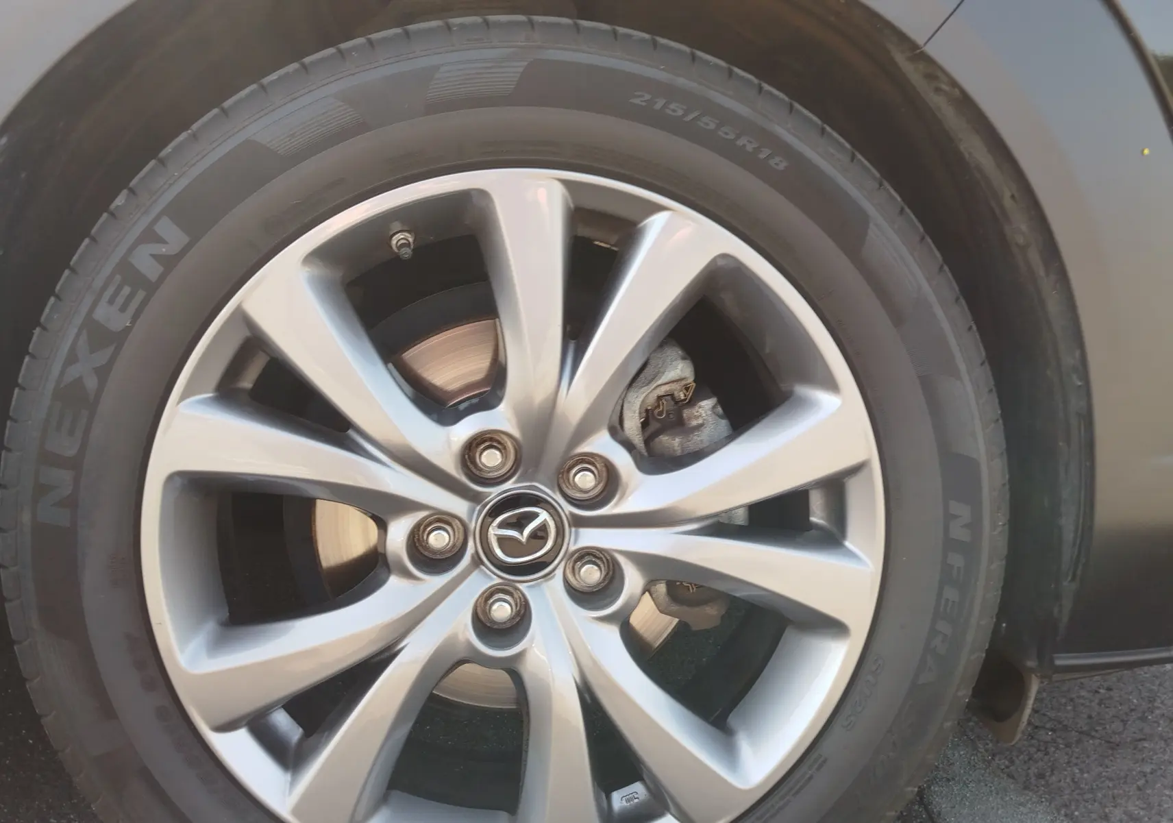 Gros plan sur la jante alliage argentée et pneu Nexen d'un Mazda CX-30 noir, mettant en valeur le logo Mazda central.