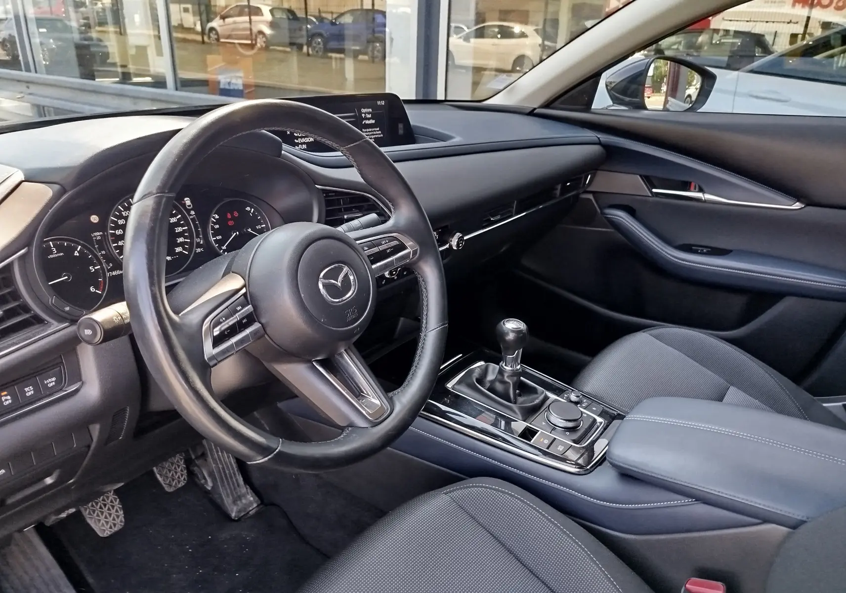 Vue intérieure côté conducteur du Mazda CX-30 2020 noir, avec volant multifonction et levier de vitesses manuel.