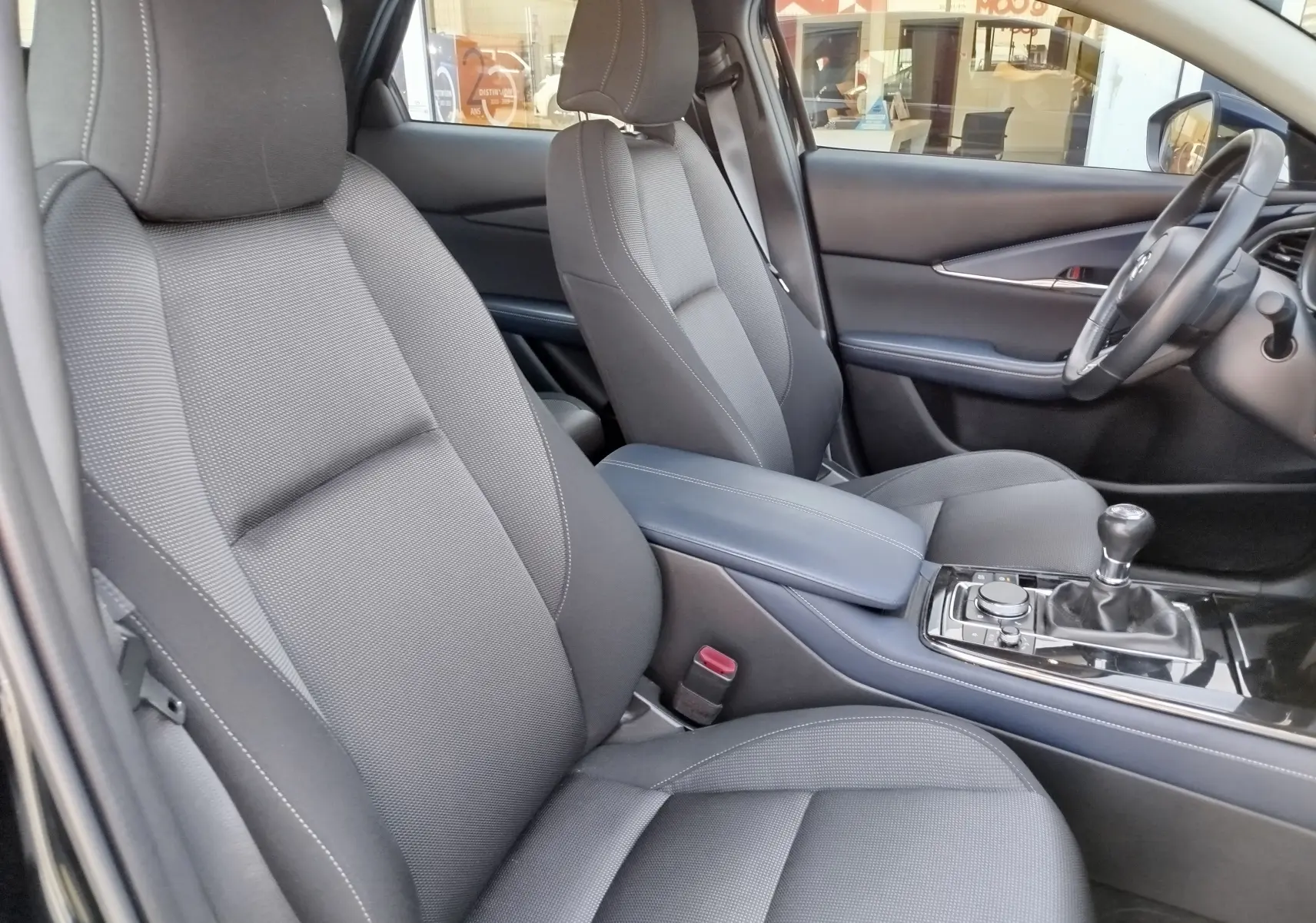 Vue intérieure côté conducteur du Mazda CX-30 noir 2020, sièges tissu noir et levier de vitesses manuel visible.