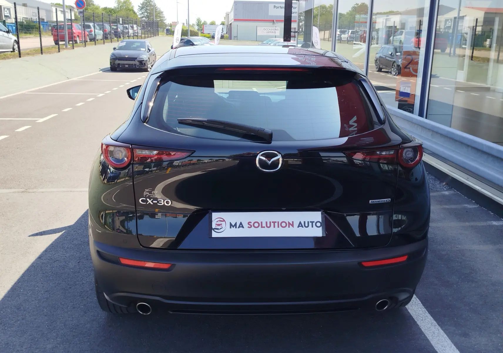 Vue arrière d'un Mazda CX-30 noir 2020 avec logo Mazda et badges CX-30 et SKYACTIV-D visibles sur un parking.