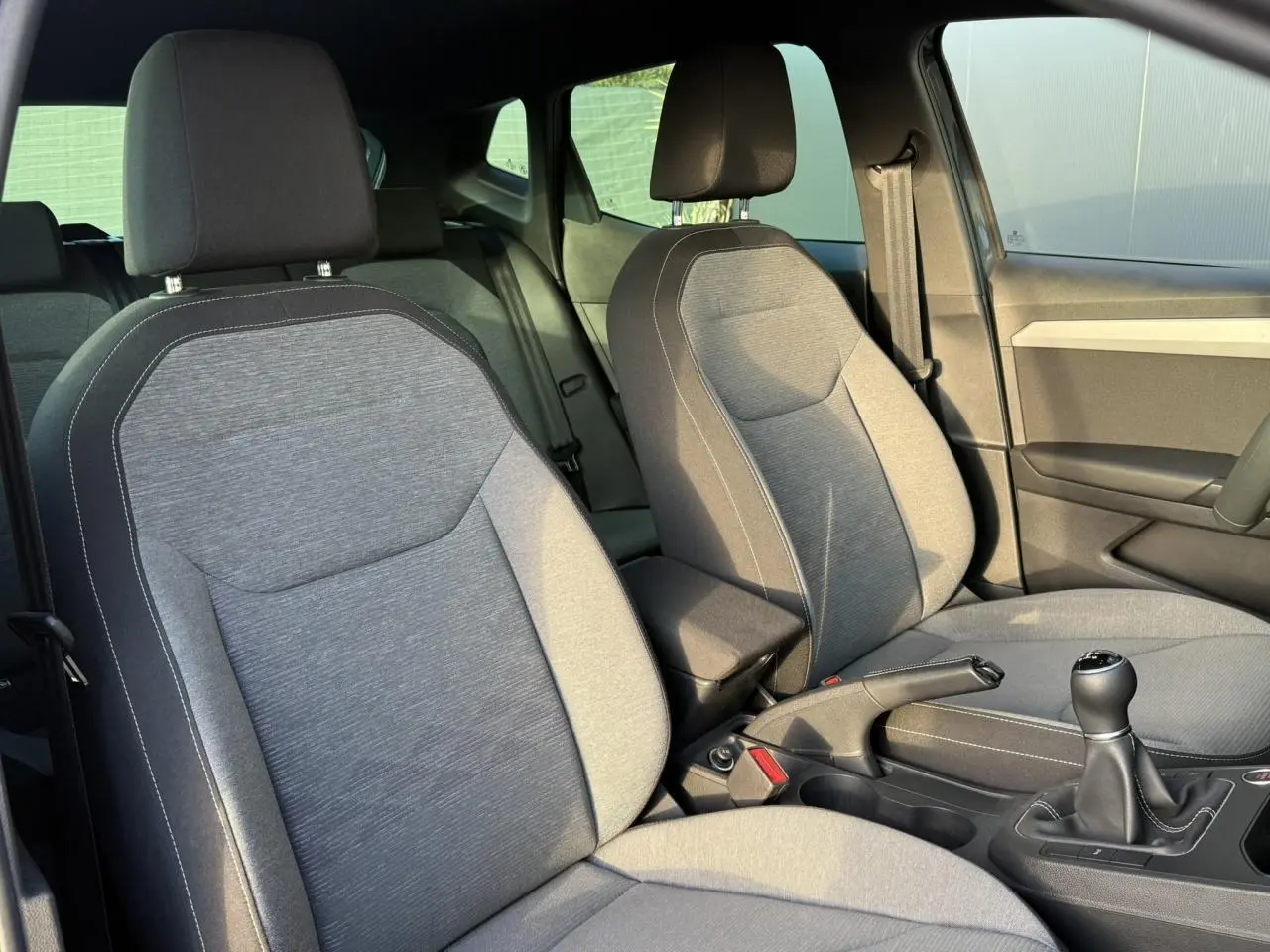 Vue intérieure rapprochée des sièges avant gris clair et console centrale d'une SEAT Ibiza TSI 115 Xcellence 2025 avec boîte manuelle.