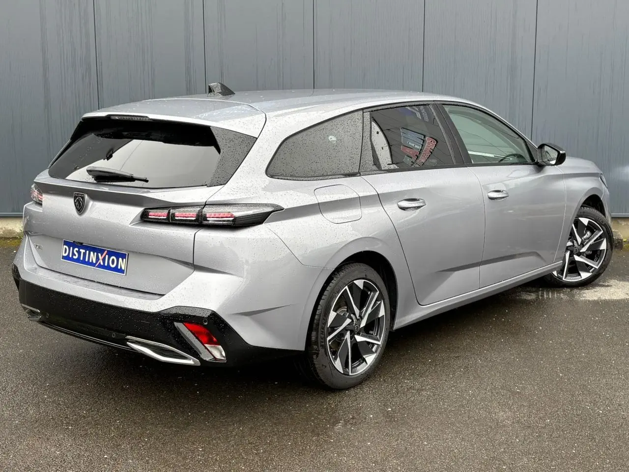 Vue 3/4 arrière droite d'une Peugeot 308 SW Hybrid gris Artense avec jantes alliage et vitres surteintées.