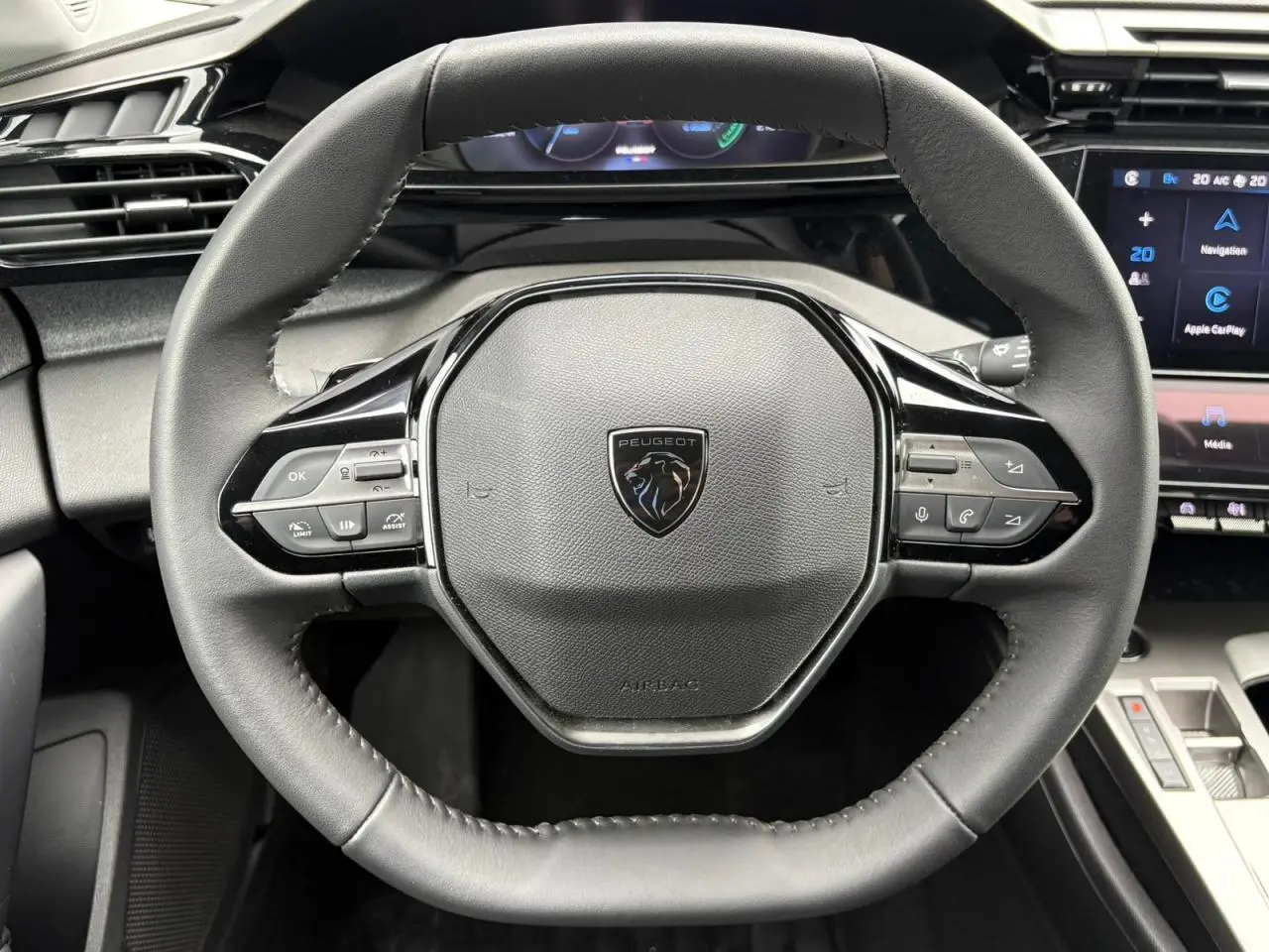 Gros plan sur le volant cuir noir du Peugeot 308 SW Hybrid 2025 avec commandes intégrées et tableau de bord numérique.