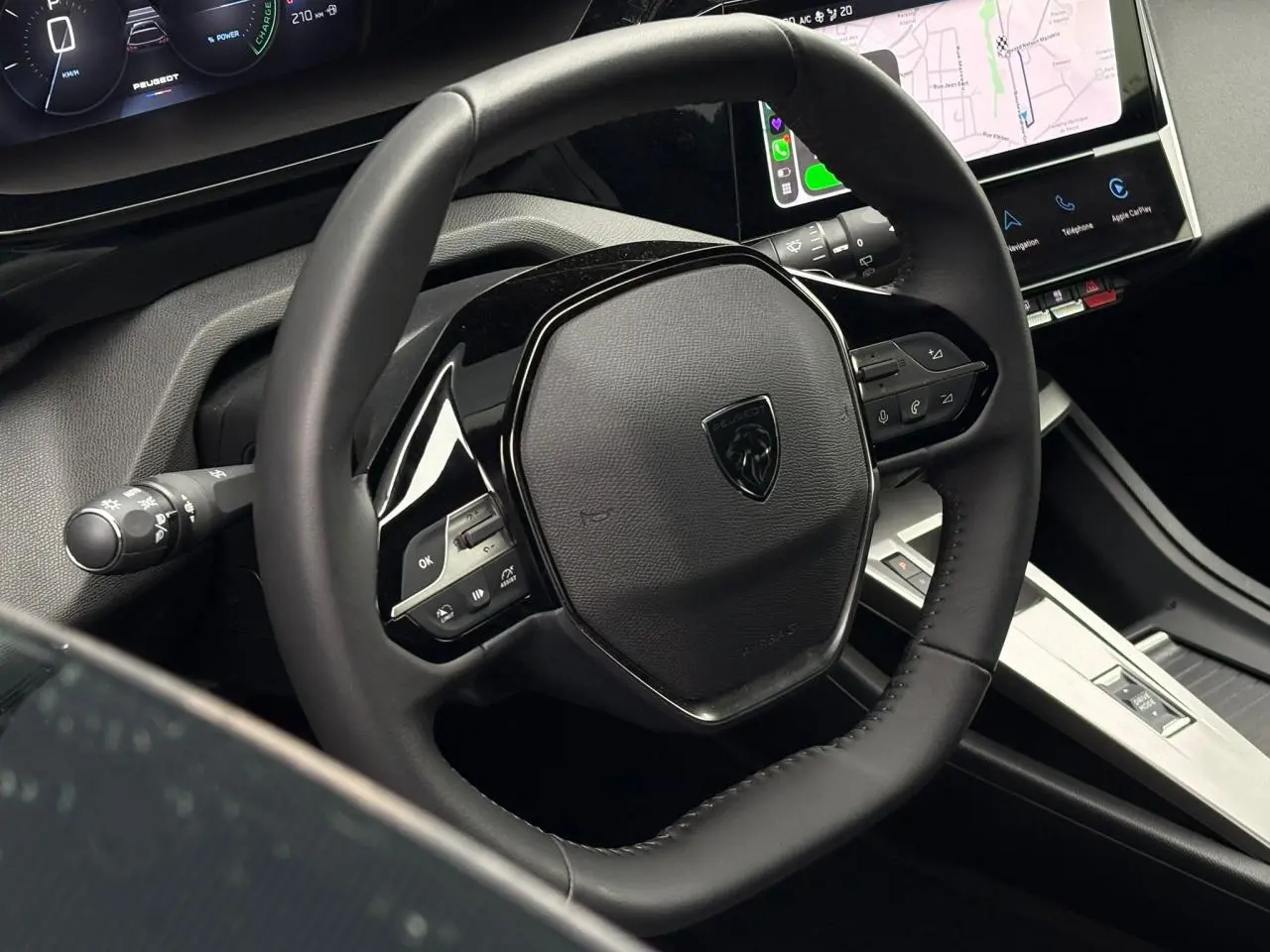Vue rapprochée du volant en cuir noir et de l'écran tactile central du Peugeot 308 SW Hybrid 2025.