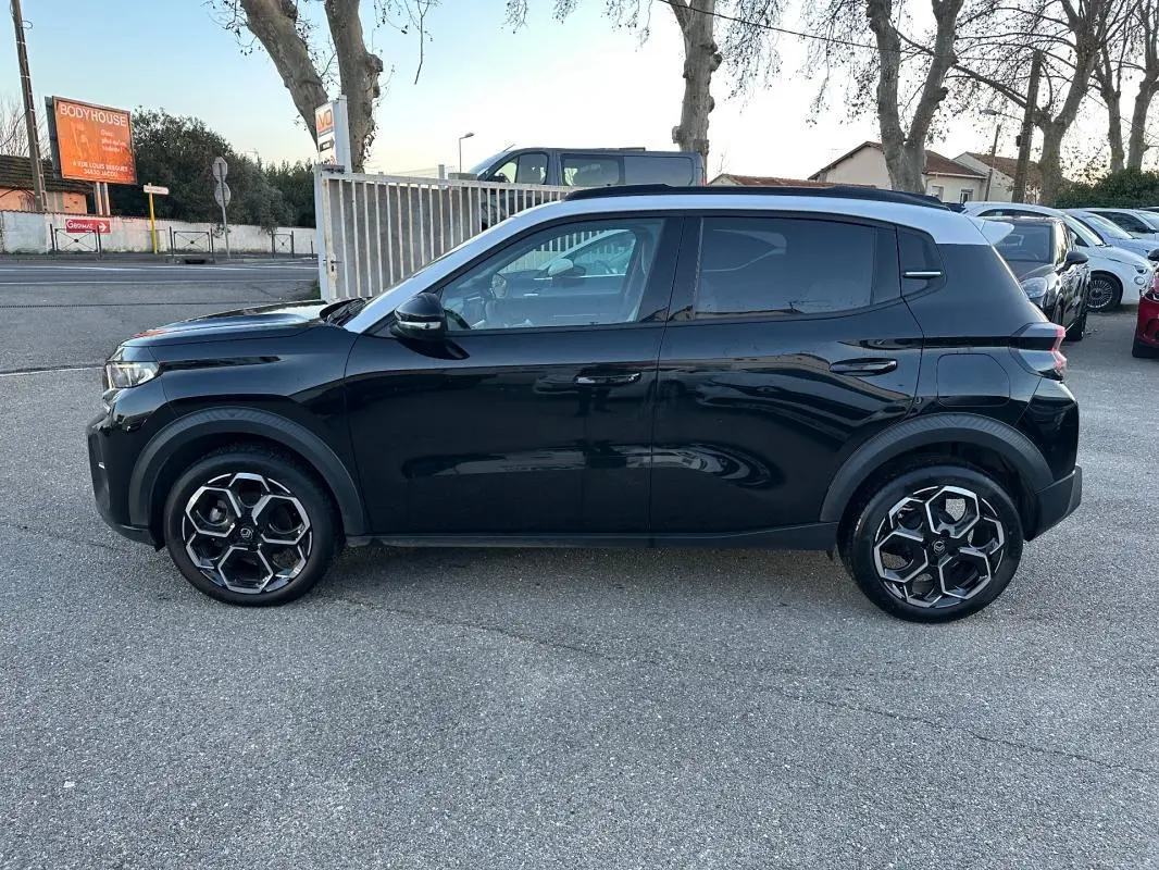 Profil côté gauche d'une Citroën C3 noire 2025 avec toit blanc et jantes alliage 17 pouces, stationnée en extérieur.