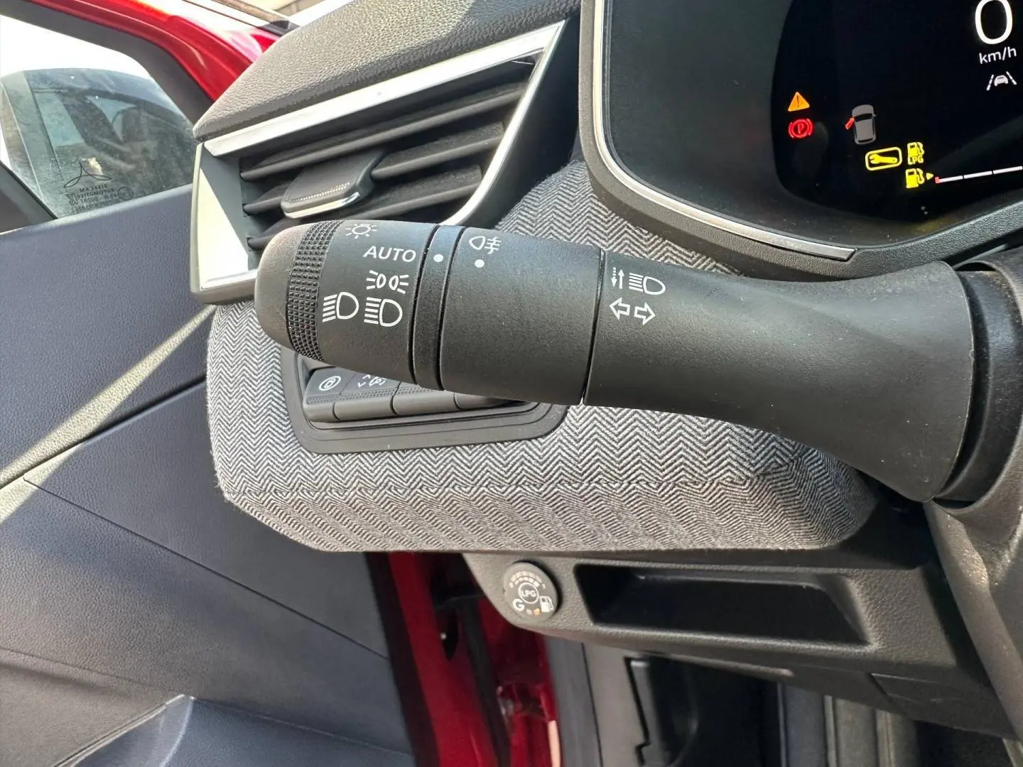 Gros plan sur la commande des phares à gauche du volant dans l’habitacle rouge flamme de la Renault Clio 2025.