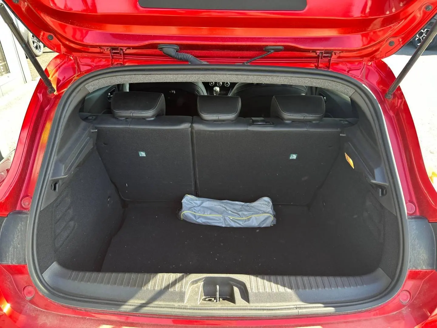 Coffre ouvert vue arrière d'une Renault Clio Rouge Flamme 2025, banquette arrière noire et tapis de coffre vide.