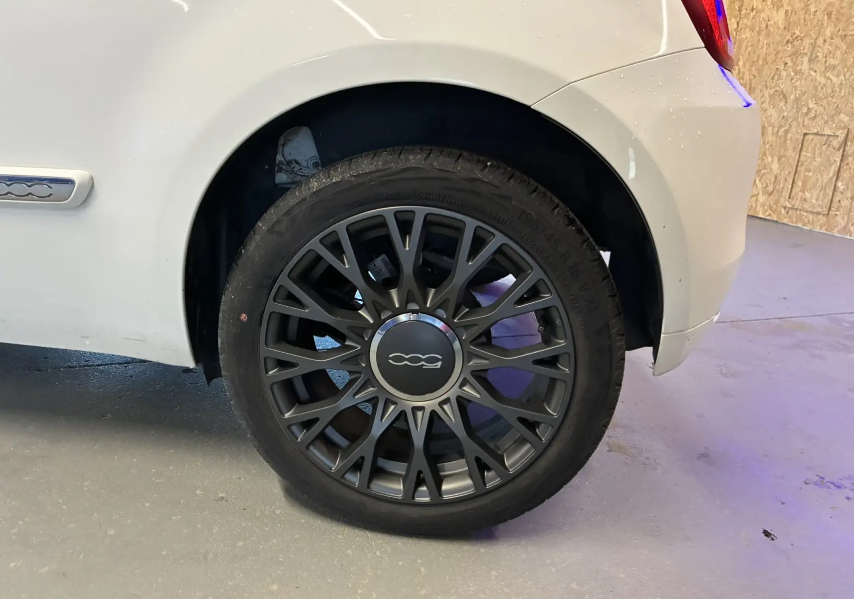 Gros plan sur la roue arrière droite d'une FIAT 500 blanche de 2021 avec jante noire au design ajouré.