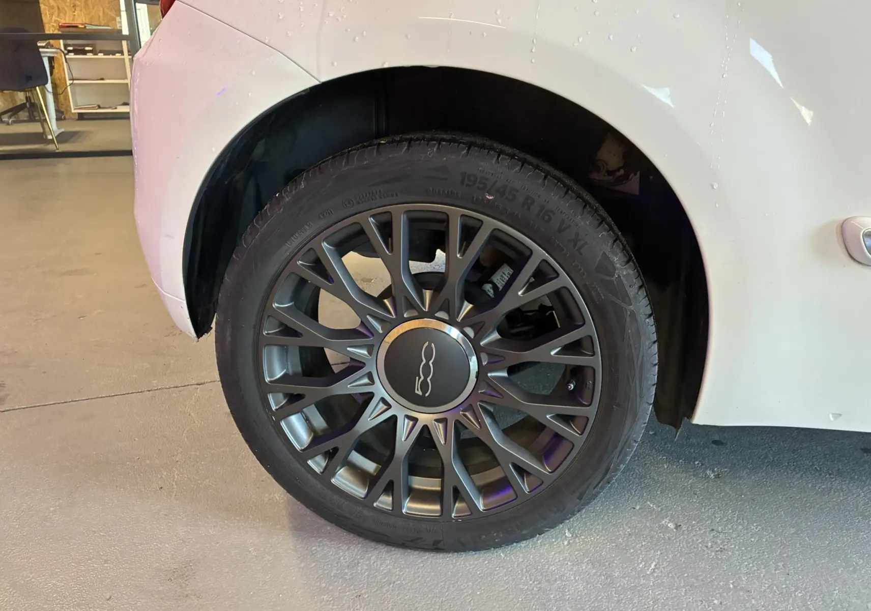 Gros plan sur la roue arrière droite d'une Fiat 500 blanche, mettant en valeur la jante alliage au design étoilé.