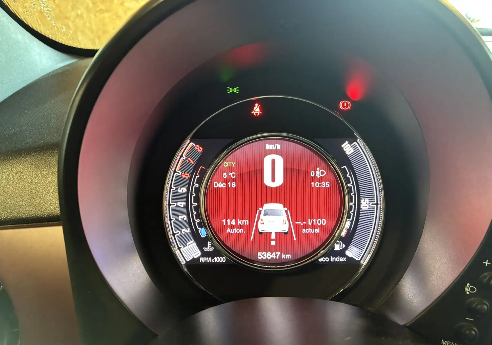 Vue rapprochée du tableau de bord numérique d'une FIAT 500 blanche, affichant la vitesse à 0 km/h et divers indicateurs.