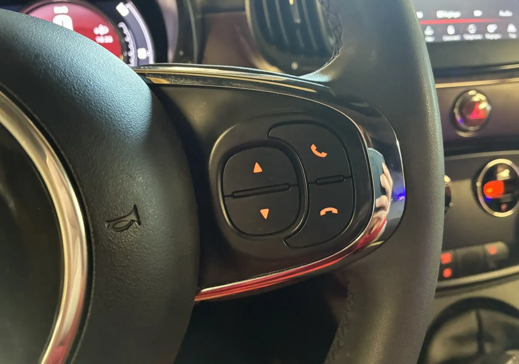 Gros plan sur les commandes du volant côté droit de la Fiat 500 blanche, avec tableau de bord et console en arrière-plan.