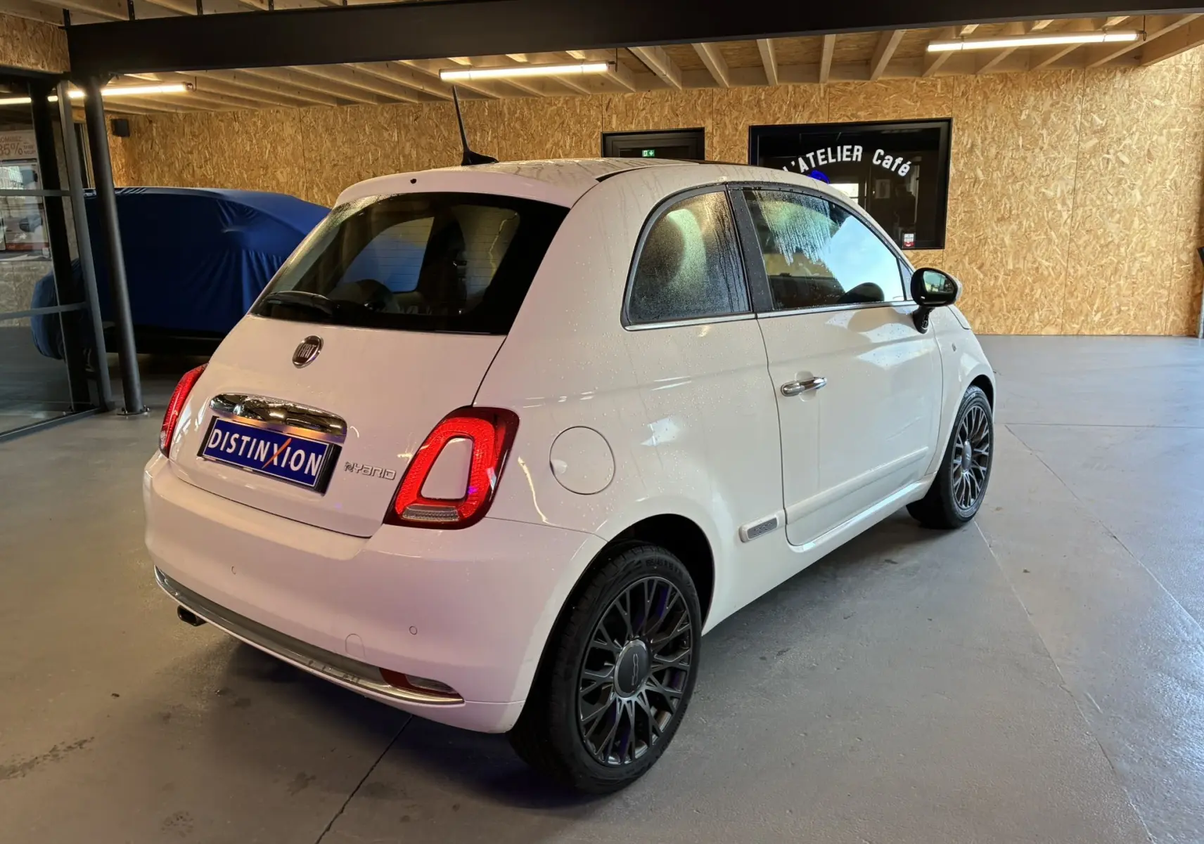 Vue 3/4 arrière droite d'une FIAT 500 blanche 2021, avec jantes noires et feux arrière allumés en intérieur.