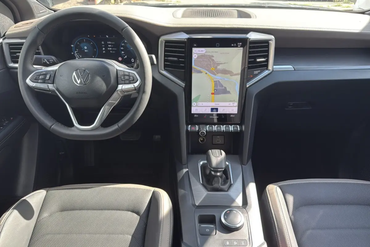 Vue intérieure avant du Volkswagen Amarok Aventura 2025, tableau de bord noir avec écran tactile central et volant cuir multifonctions.