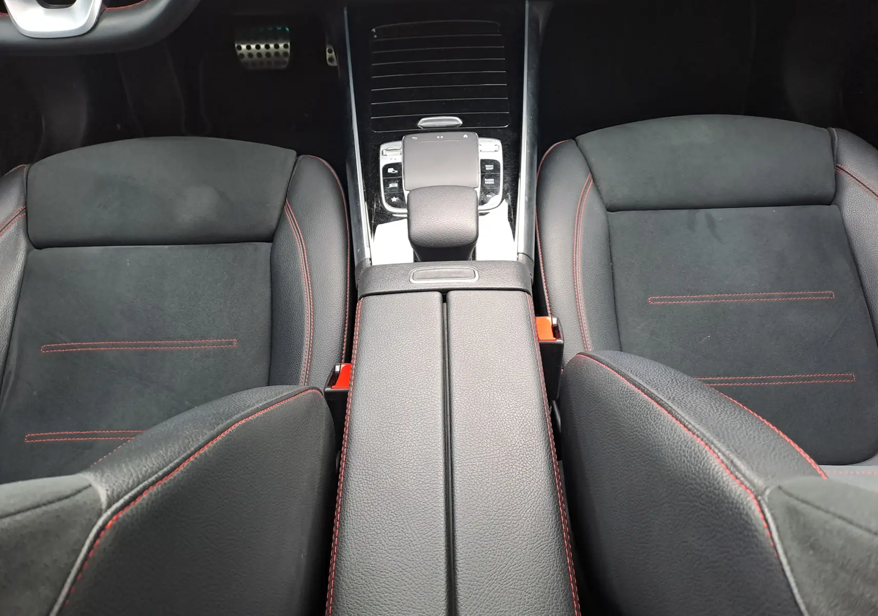 Vue intérieure centrée sur les sièges avant noirs avec surpiqûres rouges et la console centrale d'une Mercedes Classe B AMG Line 2019.