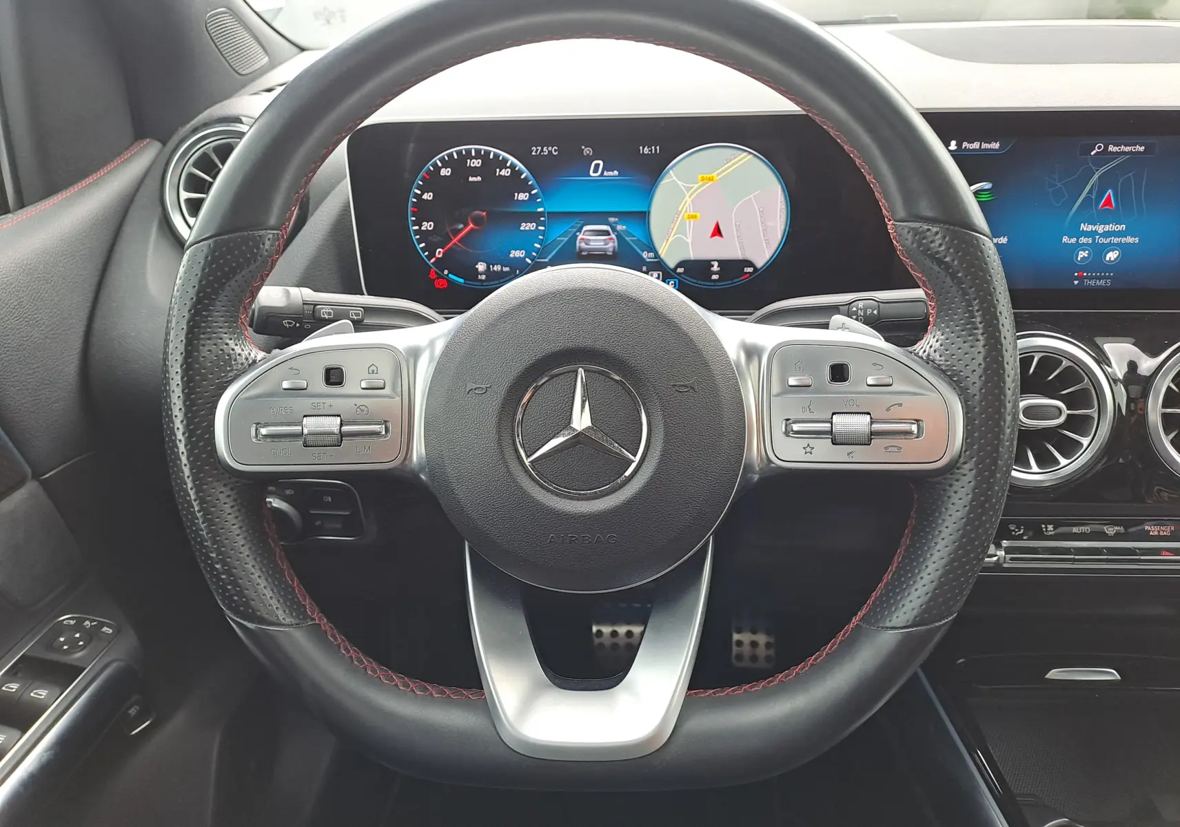 Vue rapprochée du volant cuir noir avec surpiqûres rouges et tableau de bord numérique d'une Mercedes Classe B AMG Line 2019.