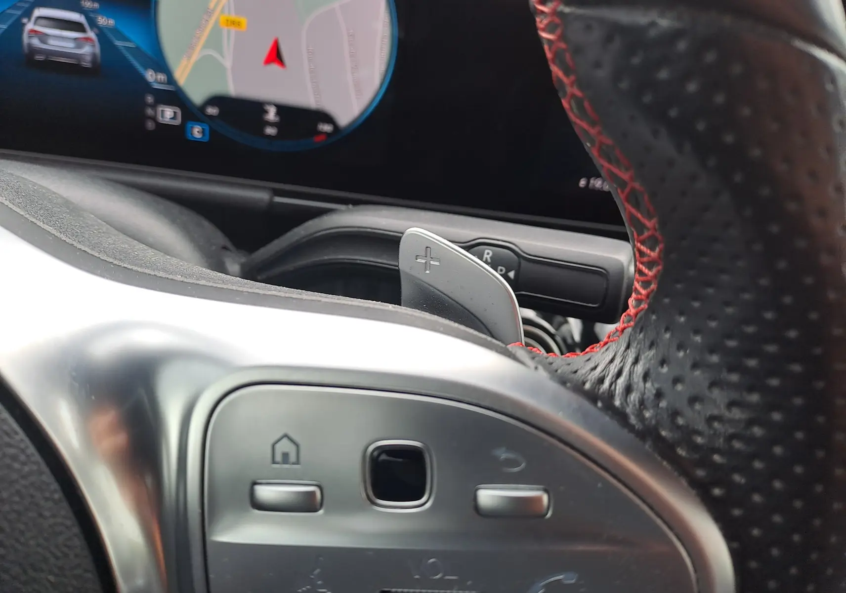 Détail du volant en cuir noir avec surpiqûres rouges et commandes intégrées, tableau de bord numérique en arrière-plan.