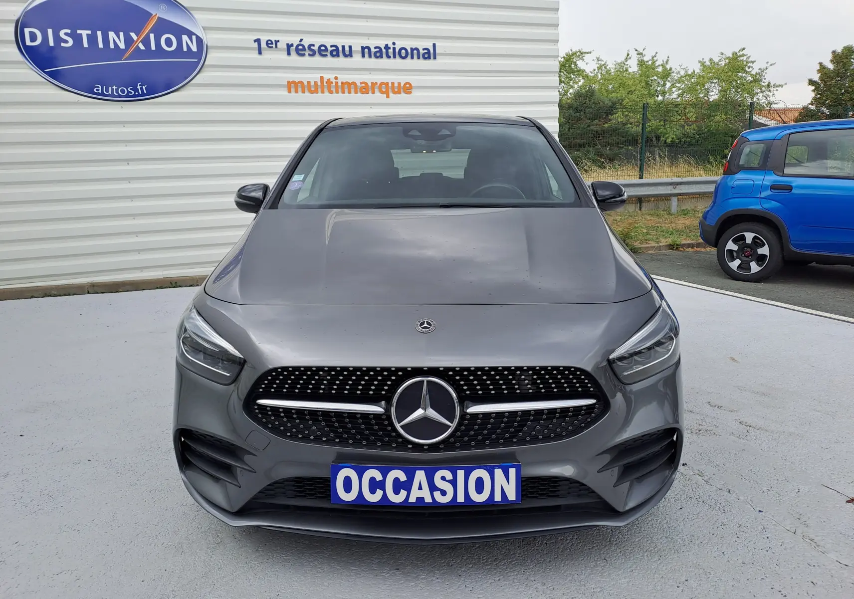 Vue de face d'une Mercedes Classe B 1.3i AMG Line gris foncé métal avec calandre distinctive et plaque "OCCASION".