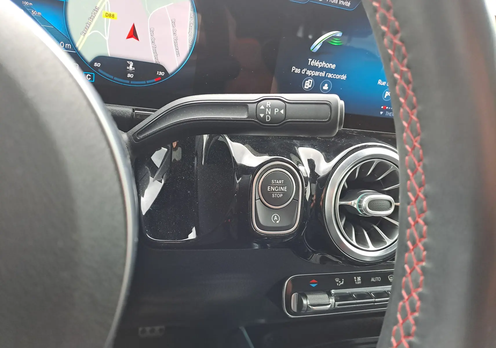 Détail intérieur montrant le bouton start/stop et la commande de boîte automatique sur fond noir brillant d'une Mercedes Classe B gris foncé.