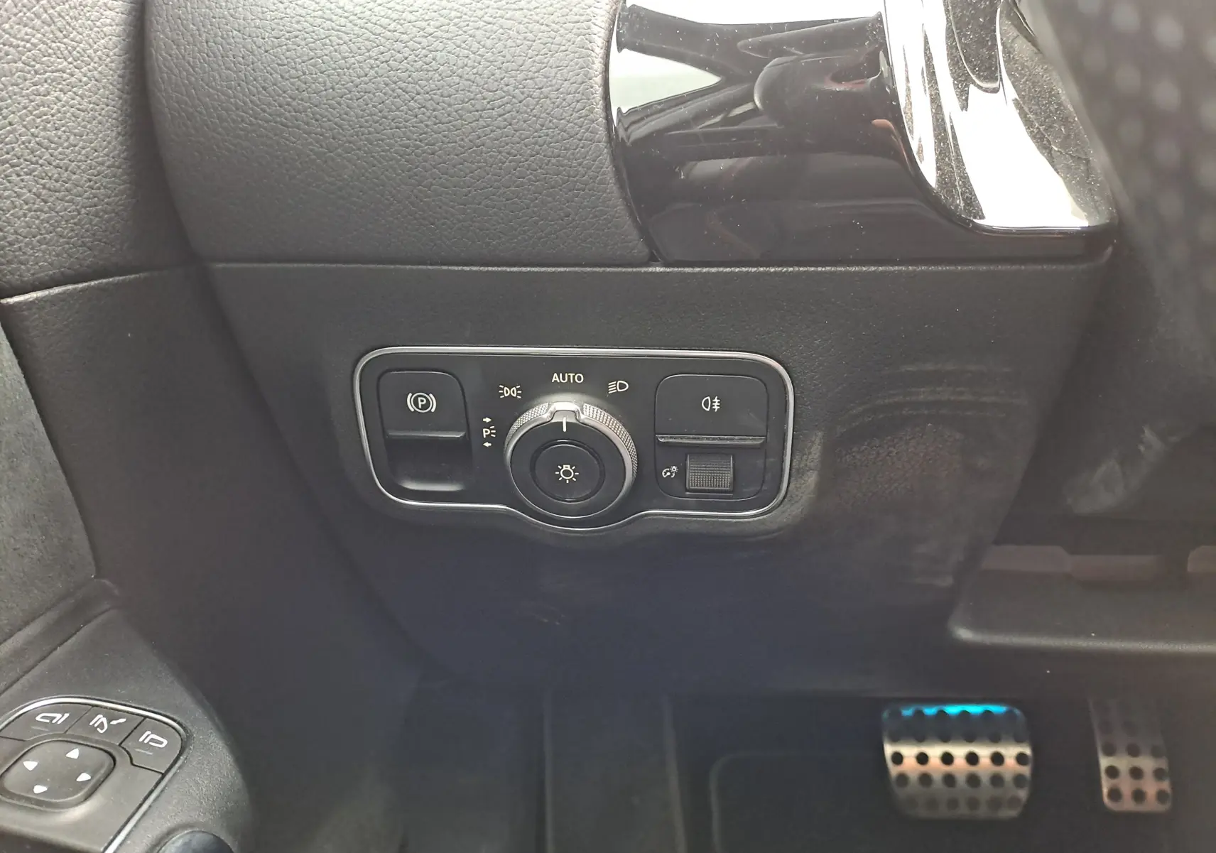 Gros plan sur le panneau de commande des phares et les pédales côté gauche d'une Mercedes Classe B gris foncé AMG Line 2019.