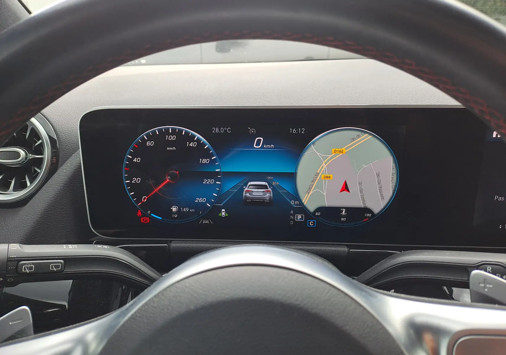 Vue depuis le poste de conduite d'un Mercedes Classe B gris foncé, affichage numérique avec compteur et navigation.