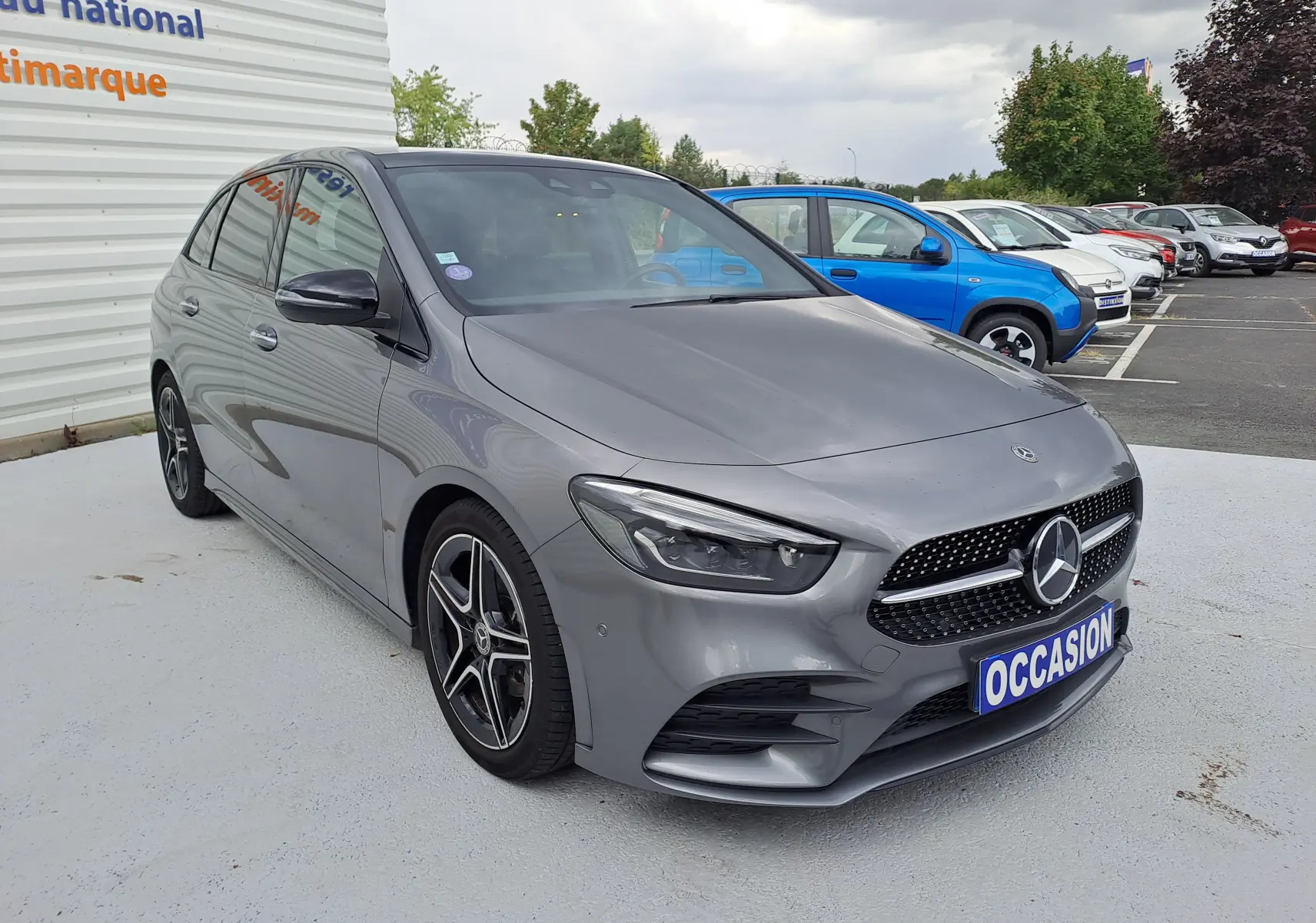 Mercedes Classe B 1.3i AMG Line gris foncé métal vue 3/4 avant avec jantes alliage et calandre sport distinctive.