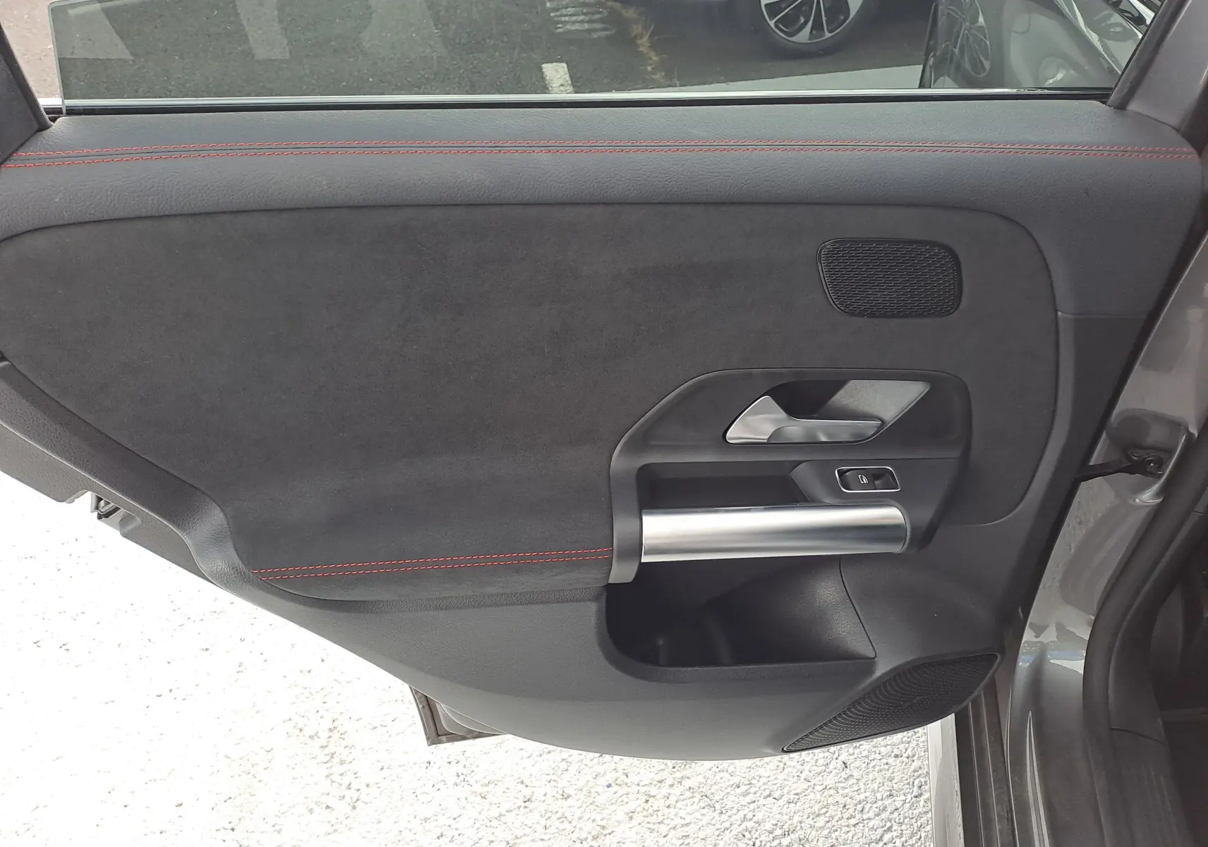 Gros plan sur la porte arrière gauche d'une Mercedes Classe B AMG Line 2019 gris foncé, avec surpiqûres rouges et poignée alu.