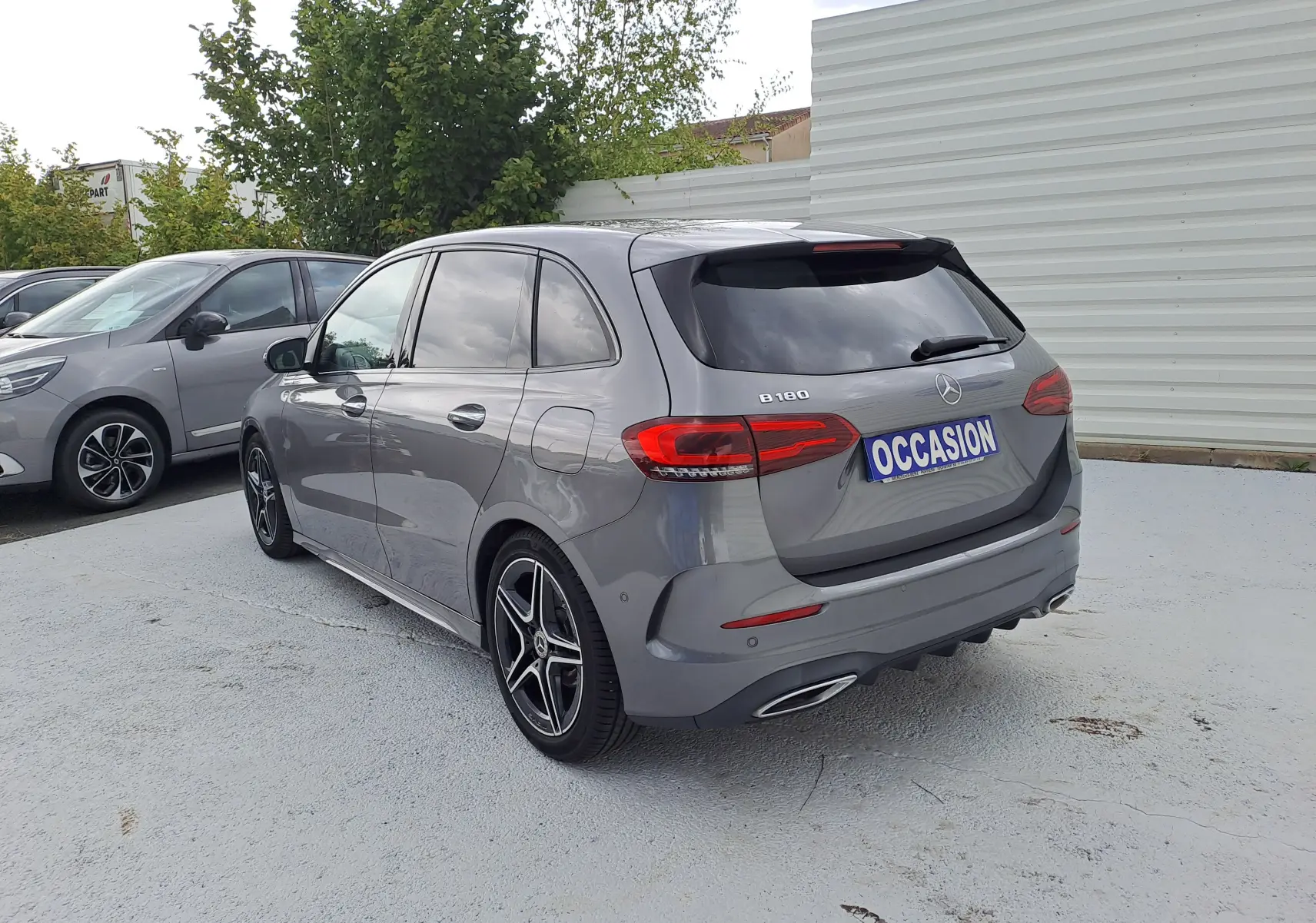 Vue 3/4 arrière droite d'une Mercedes Classe B gris foncé métal avec jantes AMG et feux LED, stationnée en extérieur.