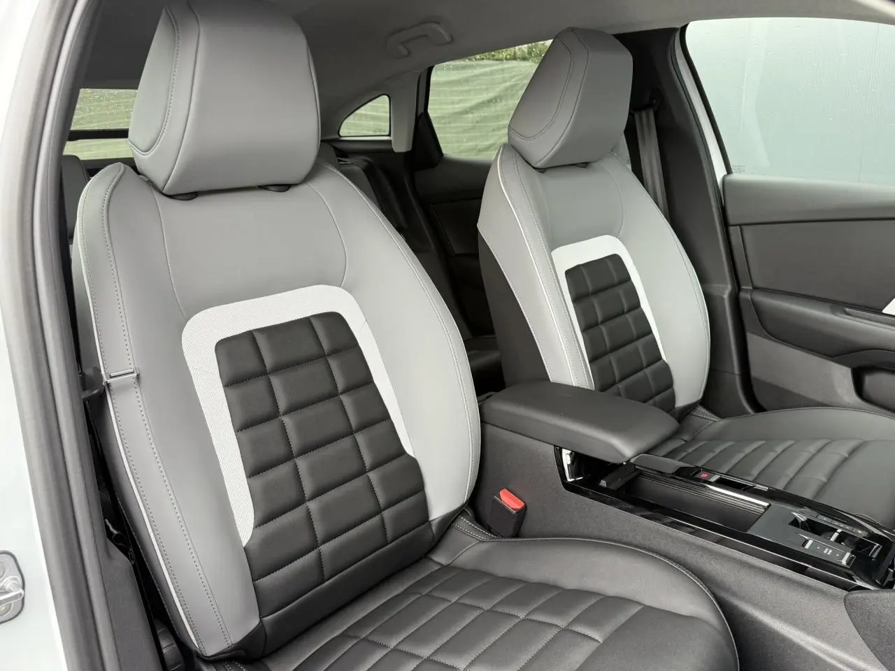 Vue intérieure des sièges avant gris clair et noir à motifs carrés du Citroën C4 NV Hybrid 2025 avec accoudoir central.