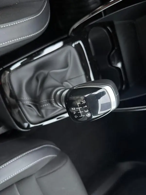 Gros plan sur le levier de vitesse manuel noir de la Citroën C3 gris, entouré de sellerie noire avec surpiqûres blanches.