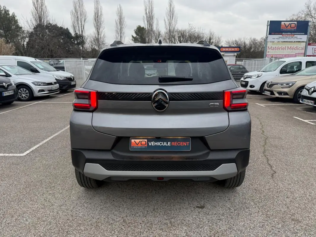 Vue arrière d'une Citroën C3 gris 2025 avec feux LED et barres de toit visibles sur parking.