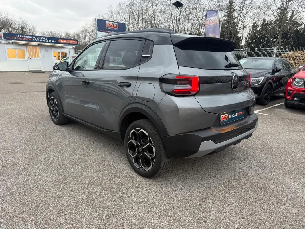 Citroën C3 gris vue 3/4 arrière droit, jantes alliage 17 pouces et barres de toit visibles.