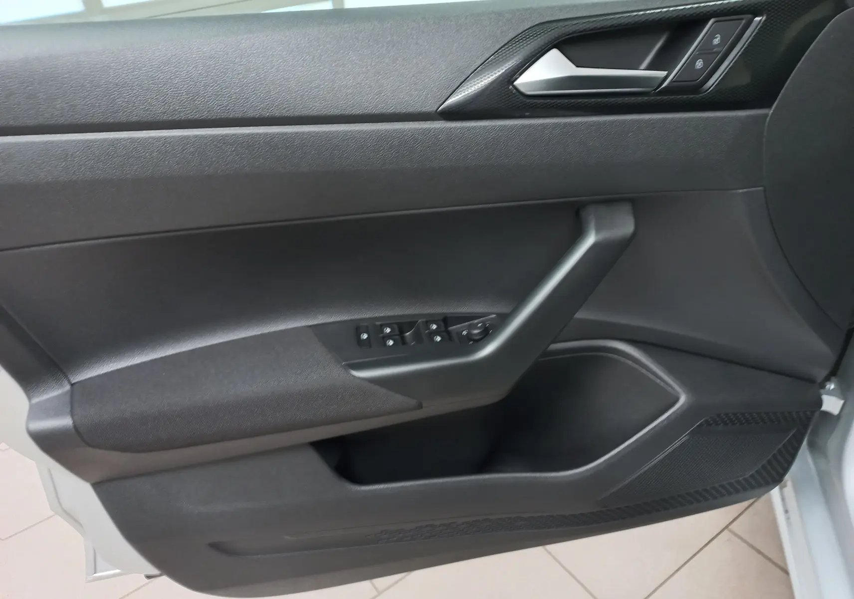 Intérieur de la porte côté conducteur d'une Volkswagen Polo 2024 reflet d'argent, avec commandes électriques et poignée noire.