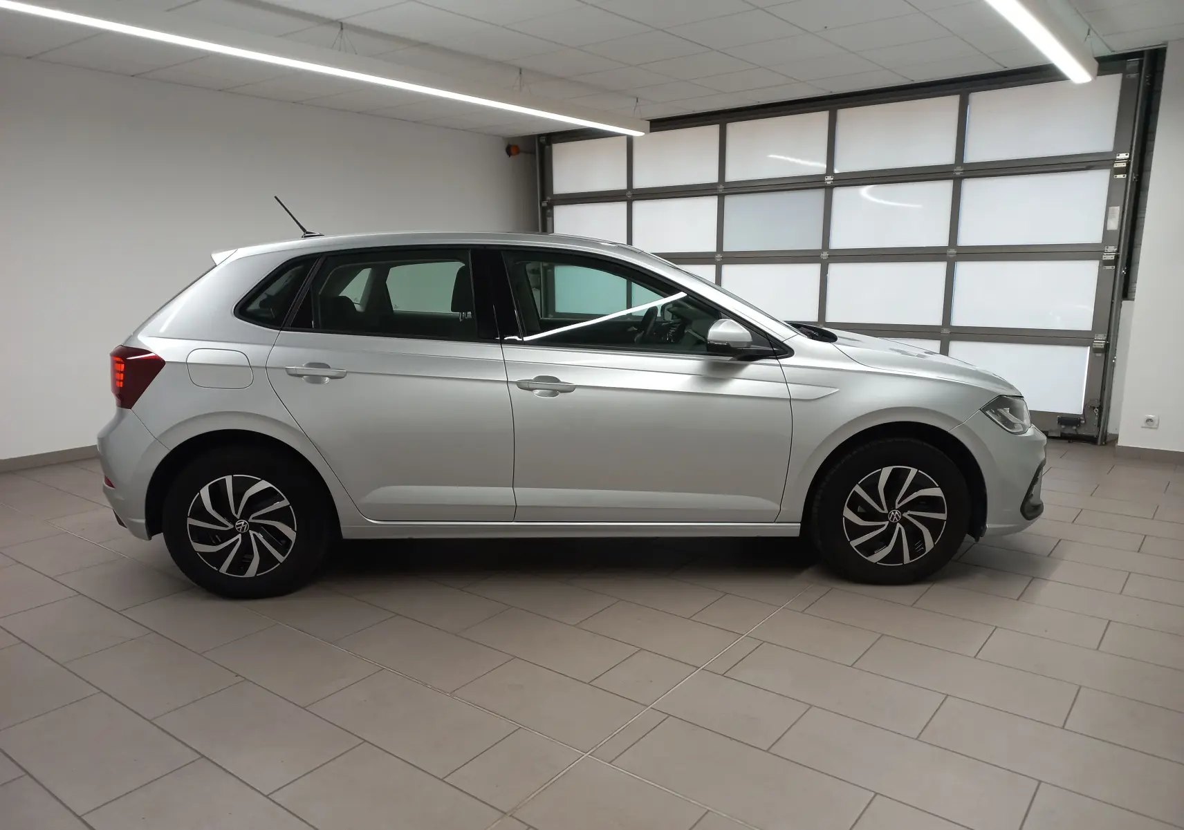 Profil côté gauche d'une Volkswagen Polo 2024 argentée, avec jantes stylisées et caméra de recul visible au-dessus du pare-chocs arrière.