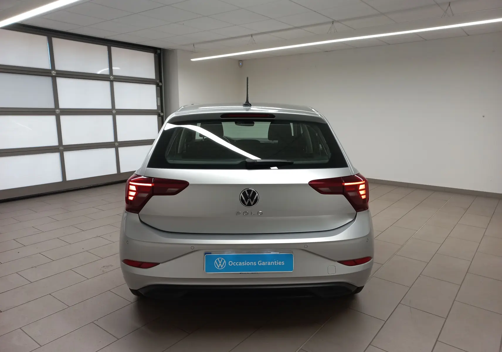 Vue arrière d'une Volkswagen Polo 2024 couleur reflet d'argent, avec feux allumés et caméra de recul visible.