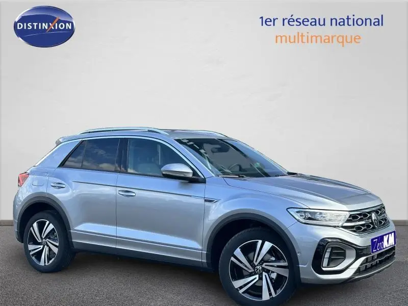 Volkswagen T-Roc 2025 gris métallisé en vue 3/4 avant droit avec jantes alliage et barres de toit.