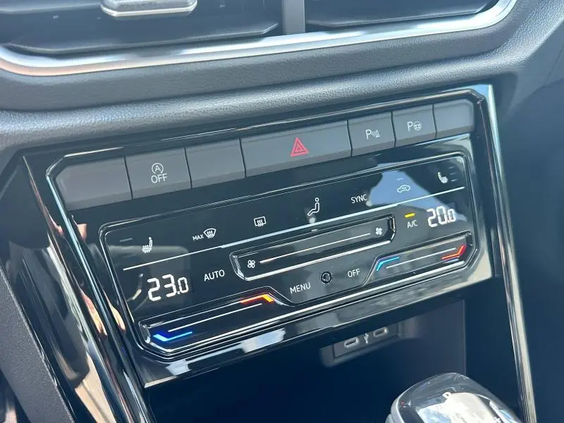 Vue rapprochée de la console centrale noire brillante du Volkswagen T-Roc 2025 avec commandes climatisation digitale et boutons d'alerte.