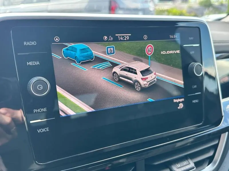 Écran tactile intérieur du Volkswagen T-Roc montrant l'aide au maintien de trajectoire avec deux véhicules stylisés en bleu et gris.