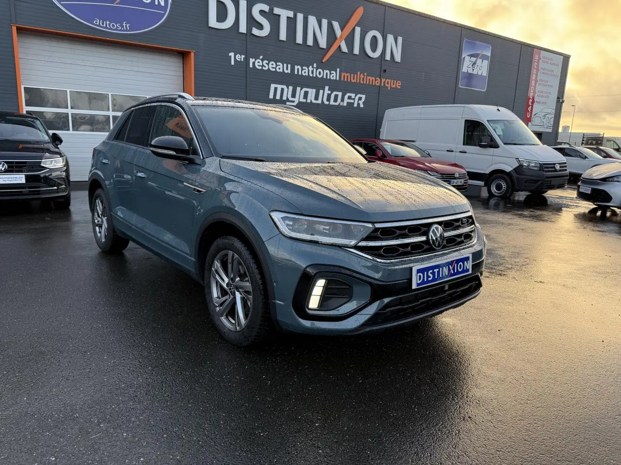 Volkswagen T-Roc bleu pétrole métallisé en 3/4 avant droit sous la pluie avec jantes alliage et feux LED allumés.