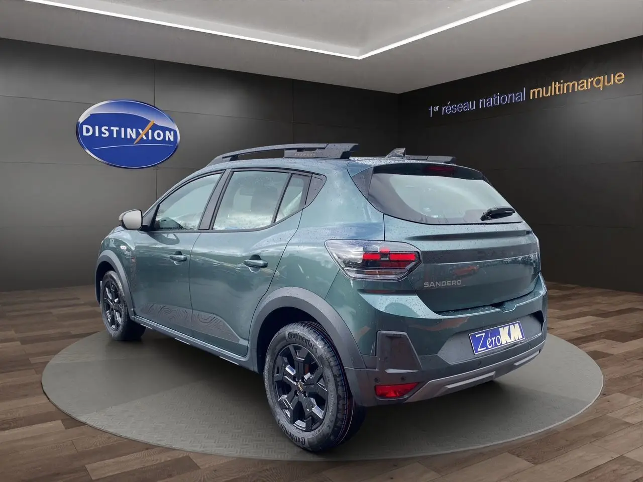 Vue 3/4 arrière droite d’une Dacia Sandero Stepway 2026 vert cèdre métallisé avec jantes alliage noires et barres de toit.